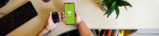 Two hands holding an Accu-Chek Guide blood glucose meter and a phone with the mySugr app