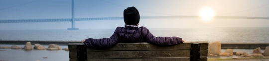 Woman sitting on a bench watching the sun set over the ocean